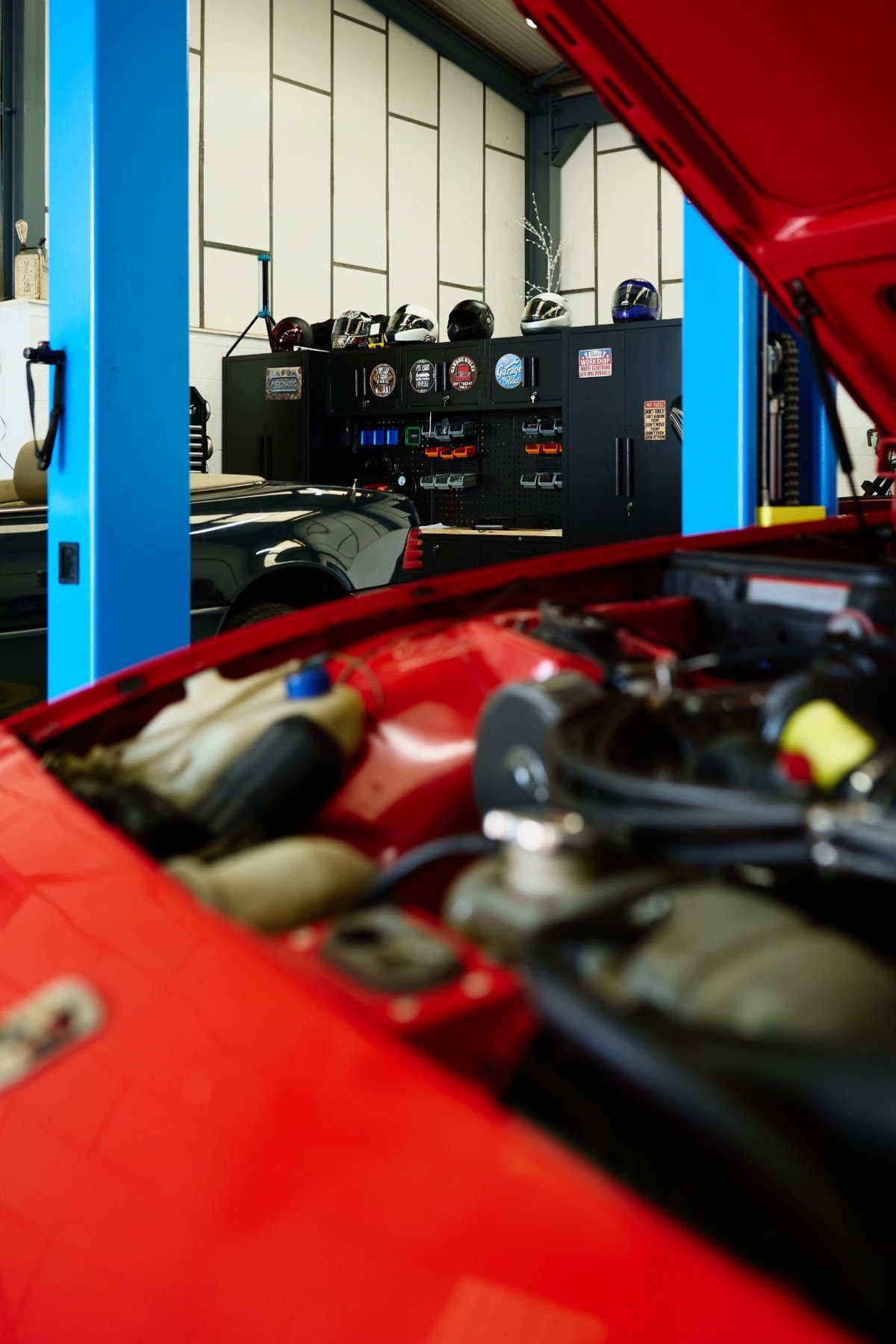 A red car with its bonnet open in front of the workshop tool cabinets