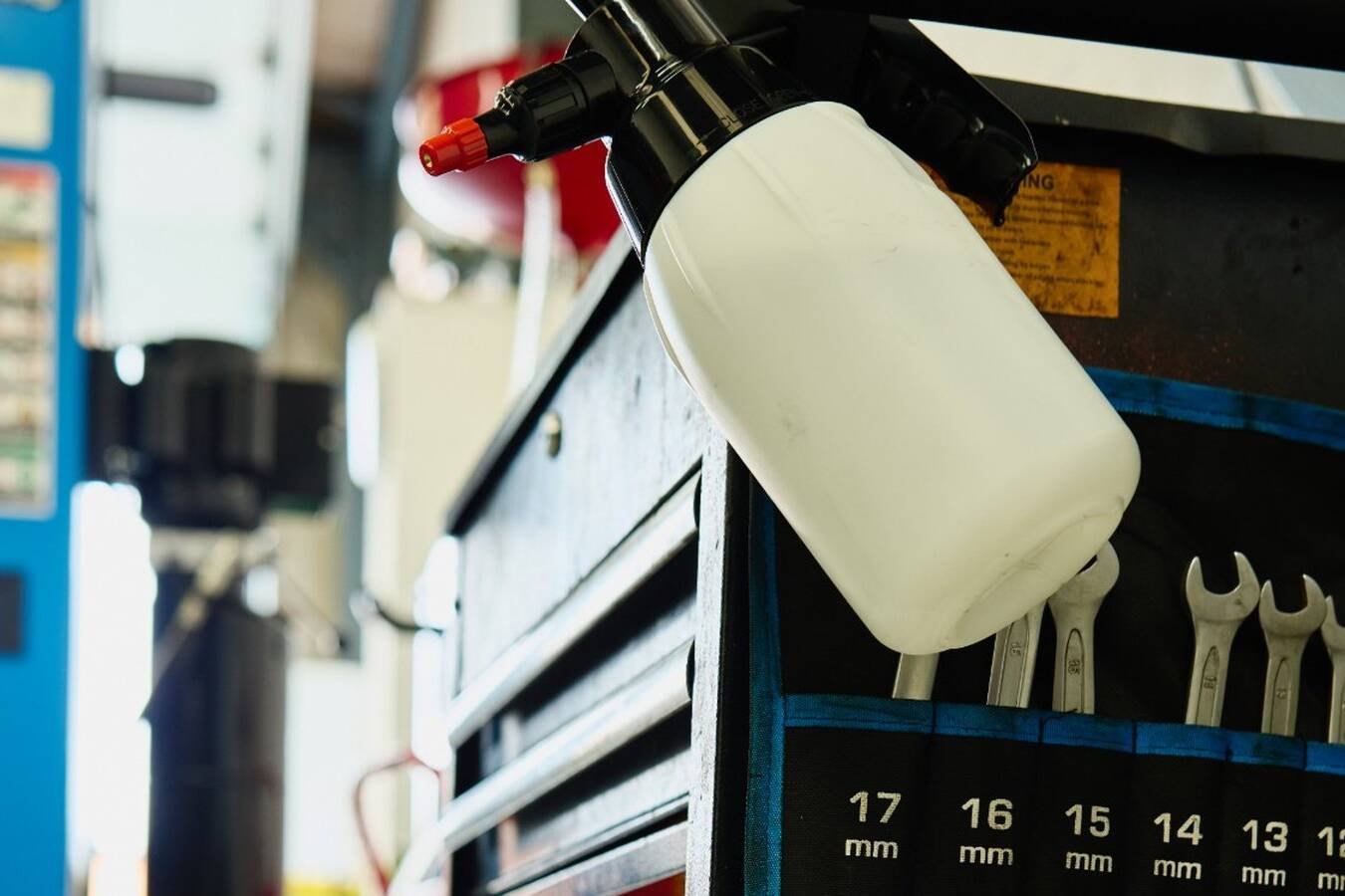 A pump sprayer hanging on a tool trolley full of spanners in a working garage